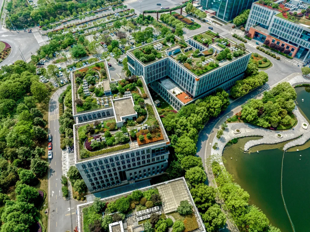 Aerial view of a modern urban area with multiple buildings featuring green rooftops, surrounded by trees and adjacent to a pond.