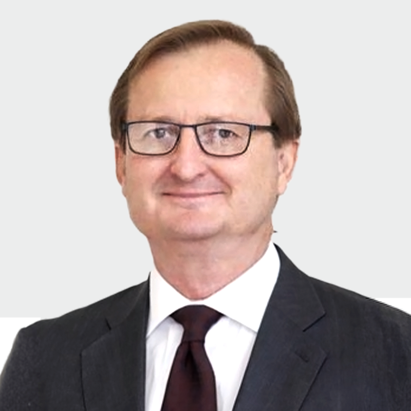 A middle-aged man with glasses, wearing a dark suit and tie, smiling slightly against a plain background.