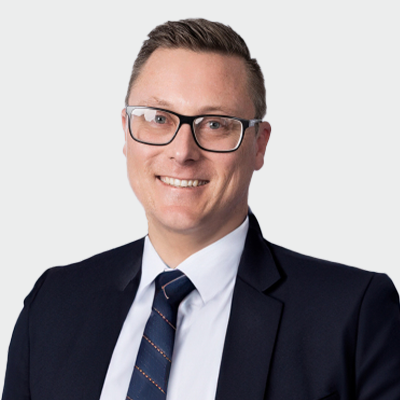 Man wearing glasses, navy suit, white shirt, and striped tie, smiling against a plain white background.