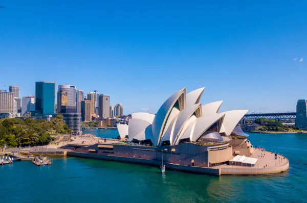 Aerial view of the Sydney Opera House with the city skyline and Sydney Harbour Bridge in the background, under a clear blue sky.